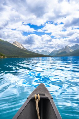 Kano, Maligne gölünün turkuaz sularında Jasper Ulusal Parkı, Alberta, Kanada 'da bulutlu mavi bir gökyüzünün altındaki Kanadalı kayalıkların çarpıcı manzarasıyla yüzüyor.