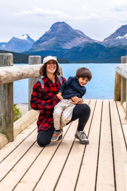 Anne, oğlunu ahşap bir köprüde tutmaktan mutluluk duyar. Pruva gölünün büyüleyici turkuaz sularının ve Kanada kayalıklarında Banff Ulusal Parkı 'nın görkemli dağlarının tadını çıkarır.