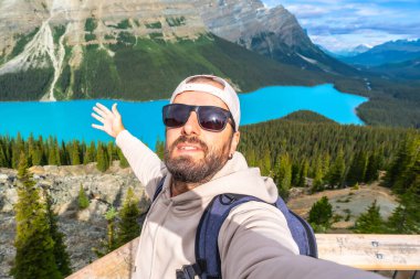 Sırt çantalı ve güneş gözlüklü bir turist, Banff Milli Parkı 'ndaki Peyton Gölü manzaralı bir yerde selfie çekiyor. Turkuaz suların ve dağların tadını çıkarıyor.