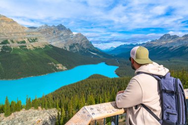 Turkuaz Peyton Gölü 'nün ve Banff Ulusal Parkı' ndaki dağların güneşli bir yaz gününde Kanadalı kayalıkların manzarasının tadını çıkaran sırt çantalı bir turist.