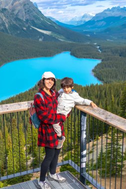 Anne, Banff Ulusal Parkı 'ndaki Peyto Gölü' ndeki görkemli dağlarla çevrili canlı turkuaz suların çarpıcı panoramik manzarasına hayran kalarak oğlunu kucağına aldı.