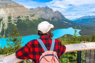 Sırt çantalı ve beyzbol şapkalı kadın turist, Turkuaz Peyton 'ın gölü ve Banff Ulusal Parkı' ndaki Kanada kayalıklarını çevreleyen nefes kesici panoramik manzarasının keyfini çıkarıyor. Alberta. Kanada mı? Yaz boyunca