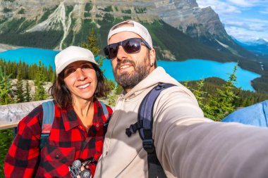 İki mutlu turist, Banff National Park, Alberta 'da güneşli bir yaz gününde, arka planda Peyton Lake ve Kanadalı kayalıklarla selfie çekiyorlar.