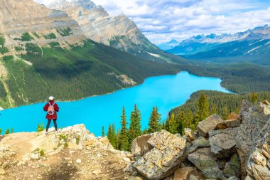 Kayalık bir uçurumda duran yürüyüşçü, Peyton Gölü 'nün turkuaz sularına bakan, Banff Milli Parkı' ndaki görkemli dağlar ve yemyeşil ormanlarla çevrili,