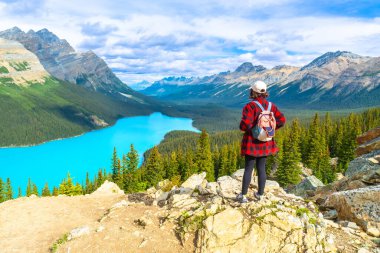 Sırt çantalı kadın turist, kayalık bir uçurumun kenarında duruyor. Peyton Gölü 'nün büyüleyici turkuaz sularına bakıyor ve Kanada' nın Banff Ulusal Parkı, Alberta, Kanada 'daki kayalık dağlarını kuşatıyor.