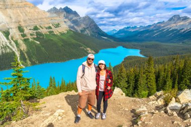 İki yürüyüşçü dağın tepesinde durmuş Peyton Gölü 'nün turkuaz sularının ve Banff Ulusal Parkı, Alberta' daki Kanada kayalarının nefes kesici manzarasının tadını çıkarıyorlar.