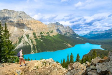 Kayalık bir çıkıntının üzerinde duran yürüyüşçü, Banff Ulusal Parkı 'nın engebeli Kanada kayalıklarına kurulmuş, Peyton Gölü' nün canlı turkuaz sularının nefes kesici manzarasını emiyor.