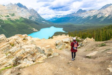 Kanadalı kayalıkların içindeki Banff Ulusal Parkı 'ndaki görkemli dağlar ve yemyeşil vadilerle çevrili Peyton Gölü' nün çarpıcı turkuaz renklerine hayran olan kadın yürüyüşçü.