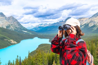 Dürbün kullanan kadın yürüyüşçü, Peyton Gölü 'nün manzaralı turkuaz sularına ve Banff Ulusal Parkı, Alberta, Kanada' daki görkemli dağlara hayran.