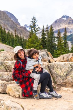 Anne ve oğlu kayaların üzerinde oturmuş turkuvaz rengi Peyton Gölü 'nün ve Banff Ulusal Parkı' nın etrafındaki dağların çarpıcı manzarasında uzun süreli anılar yaratıyorlar.