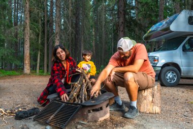 Banff Ulusal Parkı, Kanada kayalıkları, Alberta ve Kanada 'da kamp yaparken kamp arabalarının yanında kamp ateşi yakan bir aile.