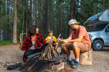 Kanadalı kayalıklarda kamp yapan aile güneşli bir yaz günü Banff Ulusal Parkı, Alberta 'da kamp ateşinin yanında kamp ateşi yakıyor.