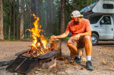Banff Ulusal Parkı 'ndaki kamp minibüsünün yanında kamp ateşi yakan turistler, Kanadalı kayalar, alberta, doğa ile çevrili barışçıl kamp deneyiminin tadını çıkarıyorlar.