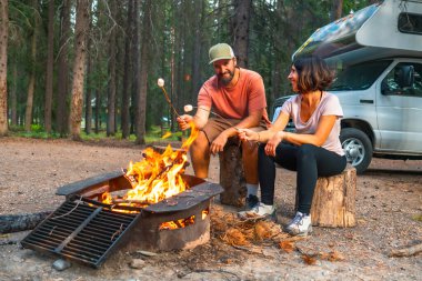 Turistler, Banff Ulusal Parkı 'ndaki kamp alanlarında kamp arabalarının yanındaki kamp ateşinde şekerleme pişiriyor ve Kanada kayalıklarında rahatlatıcı bir akşamın keyfini çıkarıyorlar.
