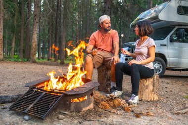 Kamp arabalarının yanındaki kamp ateşinde marşmelov kızartan turistler, Banff Ulusal Parkı 'nın vahşi doğasında huzurlu bir akşamın tadını çıkarıyorlar, Kanada kayalıkları, alberta