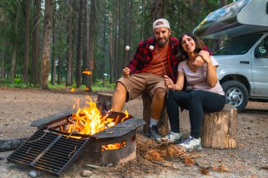 Turistler Banff Ulusal Parkı, Alberta 'da marşmelov kızartıyorlar. Kamp ateşinin yanında, Kanadalı kayaların huzur veren güzelliğiyle çevrili bir gece geçiriyorlar.