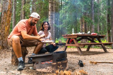 Turistler, Banff Ulusal Parkı 'ndaki kamp maceraları sırasında Alberta' nın göz kamaştırıcı kayalıklarına kurulmuş lezzetli yemekler pişirirken kamp ateşinin sıcaklığının keyfini çıkarıyorlar.