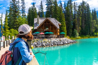 Zümrüt gölünün turkuaz sularına ve Banff Ulusal Parkı, Alberta, Kanada 'daki verimli çam ormanlarının arasına kurulmuş büyüleyici kulübesine hayran olan kadın yürüyüşçü.