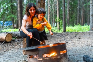 Anne ve oğlu Banff Ulusal Parkı, Alberta 'da kamp ateşinde marşmelov kızartıyorlar. Güzel Kanada kayalıkları arasında kamp gezisinin tadını çıkarıyorlar.