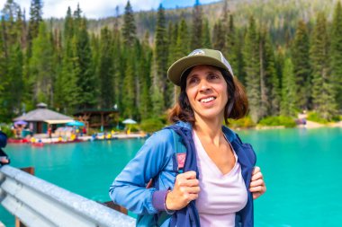 Zümrüt gölün turkuaz sularının yanında duran beyzbol şapkası ve sırt çantası takan kadın yürüyüşçü Kanada kayalıklarında, İngiliz Kolombiya 'sında Yoho Ulusal Parkı' nın manzaralı güzelliğine hayran.