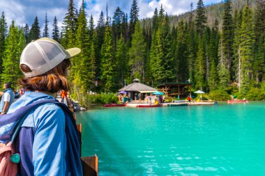 Köprüde duran turistler, Kanada kayalıklarında nefes kesici bir doğa harikası olan Banff Ulusal Parkı 'ndaki yemyeşil ormanlarla çevrili zümrüt gölünün turkuaz sularına hayran.