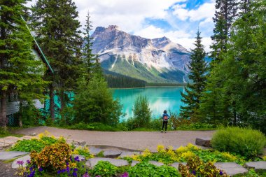 Zümrüt gölünün nefes kesici turkuaz sularına ve yemyeşil bitki örtüsü ve Banff Milli Parkı 'nda ahşap bir kulübeyle çevrili heybetli dağ evine hayran kalan bir turist.