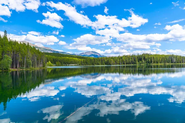 Sakin sular Herbert Gölü 'nün üzerinde, Banff Milli Parkı' ndaki gür çam ormanları ve görkemli dağlarla çevrili çarpıcı bulutlu bir gökyüzünü yansıtıyor.