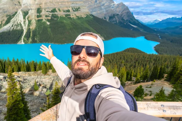 Sırt çantalı ve güneş gözlüklü bir turist, Banff Milli Parkı 'ndaki Peyton Gölü manzaralı bir yerde selfie çekiyor. Turkuaz suların ve dağların tadını çıkarıyor.