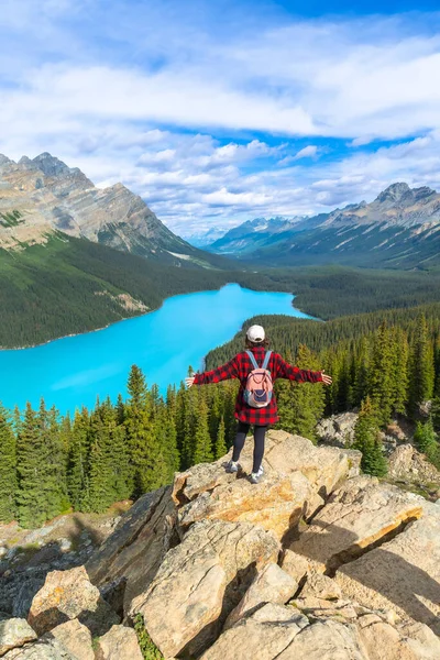 Sırt çantalı kadın yürüyüşçü kayalık bir uçurumda duruyor, Turkuaz Peyton Gölü 'nün ve Banff Ulusal Parkı' ndaki görkemli Kanada kayalıklarının muhteşem manzarasının tadını çıkarıyor.