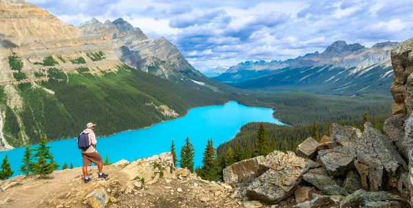 Sırt çantalı turist, bulutlu bir gökyüzü altında Banff Ulusal Parkı 'ndaki Turkuaz Peyton Gölü ve Kanadalı kayalıkların nefes kesici manzarasının keyfini çıkarıyor.