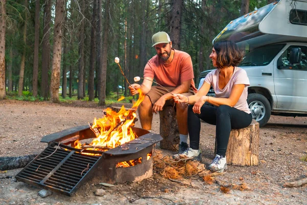 Turistler, Banff Ulusal Parkı 'ndaki kamp alanlarında kamp arabalarının yanındaki kamp ateşinde şekerleme pişiriyor ve Kanada kayalıklarında rahatlatıcı bir akşamın keyfini çıkarıyorlar.