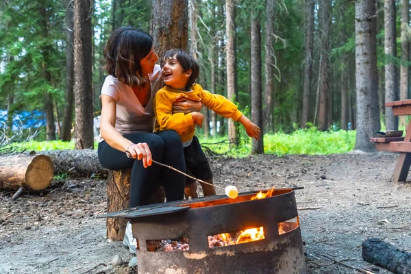 Anne ve oğlu Banff Ulusal Parkı, Alberta, Kanada 'da kamp ateşinde marşmelov kızartıyorlar. Birlikte güzel doğal ortamların tadını çıkarıyorlar.