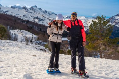 Karlı bir dağ manzarasında kar ayakkabıları giyen ve maceranın tadını çıkaran mutlu çift, eşleri tarafından desteklenen, aktif bir kış tatili yapıyorlar.