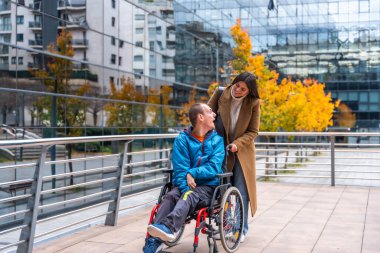Genç bir kadın bakıcı tekerlekli sandalyedeki engelli bir adamı itiyor, sonbahar boyunca şehir ortamında mutlu bir anı paylaşıyor.