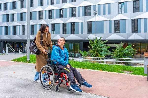 Kadın, tekerlekli sandalyedeki gülümseyen bir adamı kaldırımlı bir şehir yolunda itiyor, şehrin sokaklarında birlikte dolaşırken bir anlık bir bağlantı ve destek paylaşıyor.