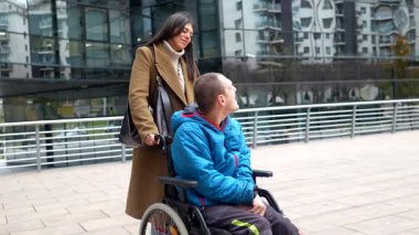 Genç bir sosyal hizmet görevlisi, engelli insanlar için bakım, destek ve sosyal katılımın önemini gösteren, modern şehir bağlamında tekerlekli sandalyede oturan engelli bir insanla yürüyüşe çıkıyor.