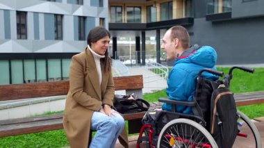 Tekerlekli sandalyede fiziksel engelli genç bir adam şehir parkında kadın bir sosyal hizmet görevlisiyle sohbet ediyor. Destek, kapsama ve pozitif iletişim gösteriyor.