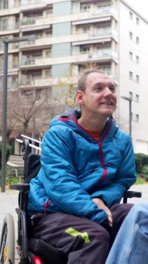 Tekerlekli sandalyede oturan genç engelli bir adam bir şehir parkında arkadaşlarıyla sohbet ediyor, dostluk ve sosyal katılımı sergiliyor.