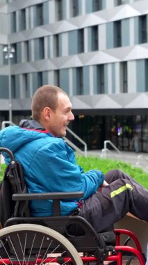 Tekerlekli sandalyedeki engelli genç beyaz adam, şehir parkında bir bankta oturan bir bayanla canlı sohbetin keyfini çıkarıyor, bir anlık bir bağ paylaşıyor ve anlıyor.