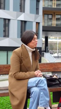 Parktaki bankta oturan genç bir kadın bakıcı tekerlekli sandalyedeki fiziksel engelli bir adamla mutlu bir şekilde sohbet ediyor. Şehir ortamında destekleyici ve arkadaşça bir sohbetten zevk alıyor.