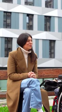 Parktaki bankta oturan şefkatli kadın engelli, tekerlekli sandalye kullanan, empati gösteren ve sosyal içeriği olan genç bir adamla çekici ve destekleyici bir konuşma yapıyor.