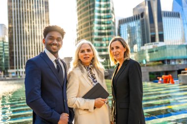 Günbatımında ofis binaları ile modern bir kentsel çevrede birleşmiş, gülümseyen, işbirliği ve başarı sergileyen çeşitli profesyonel iş ekipleri