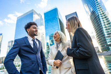 Modern kurumsal binaların önündeki projeleri, şehir ortamında takım çalışmasını, küresel ortaklığı ve kariyer büyümesini sembolize eden çeşitli iş profesyonelleri iletişim kuruyor ve tartışıyorlar.