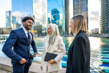 Çeşitli iş adamları dinamik gayri resmi bir toplantı yapıyorlar ve modern bir şehir ortamında fikirleri tartışıyorlar. Gökdelenler suya yansıyor.
