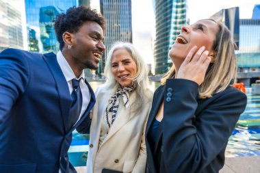 Çeşitli yaşlardan ve etnik kökenlerden mutlu iş adamları modern gökdelenlerle dolu bir şehir ortamında takım çalışmasını, başarıyı ve pozitif kurumsal kültürü temsil ederek birlikte gülüyorlar.