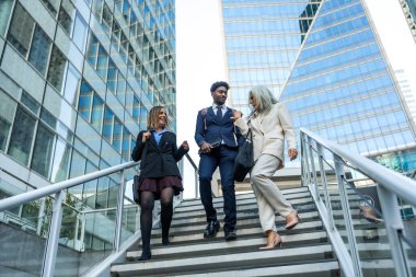 Çeşitli iş arkadaşları modern bir finans bölgesinde açık merdivenlerden inerek, cam gökdelenler arasında sohbet ve işbirliği içinde hareket halindeki profesyonellere ve kentsel takım çalışmasına güveniyorlar.