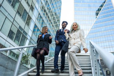 Modern bir finans bölgesinde merdivenlerden aşağı inen çeşitli iş adamları topluluğu iş ve şehir ortamında işbirliği yapıyorlar.