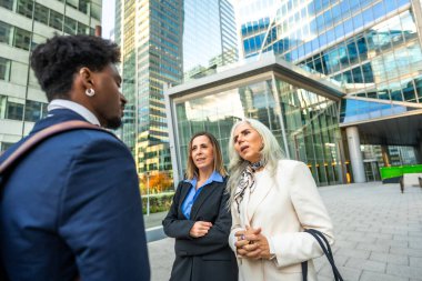 Çeşitli iş adamları gayri resmi bir açık hava toplantısı yapıyor, fikirleri tartışıyor ve ofis binalarıyla modern şehir ortamında bir proje üzerinde işbirliği yapıyorlar.