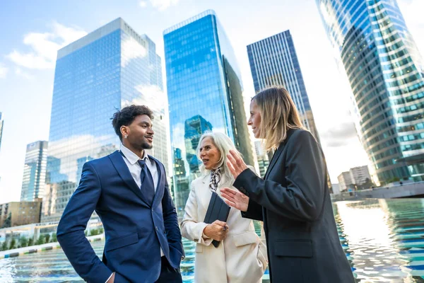 Resmi giysiler içinde çeşitli iş adamları iş ve açık havada işbirliği yapıyor, takım çalışması ve modern şehir gökdelenleri ile kurumsal başarıyı arka planda yansıtıyor