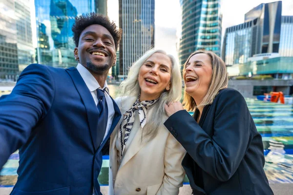 Çeşitli iş adamları birlikte selfie çekerken, takım çalışması, işbirliği ve modern bir şehir ortamında pozitif çalışma ortamı sergilerken mutlu ve başarıyı kutluyorlar.
